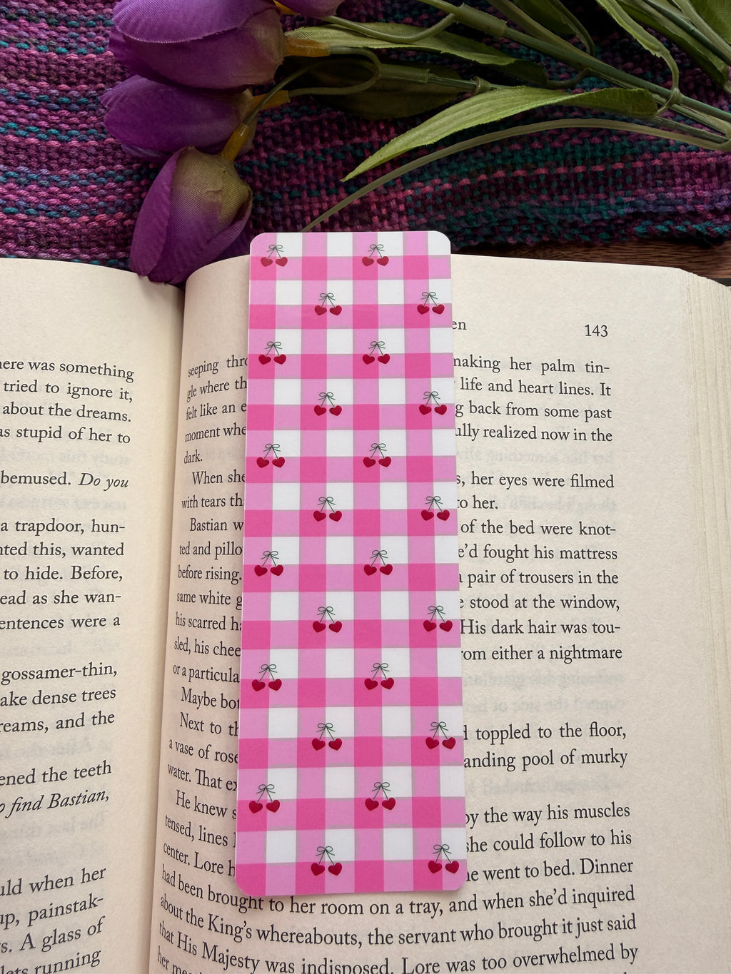 Pink checkered bookmark on an open book with a purple flower and green leaves.